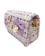 Side view of the little girls purple tweed purse showing the purple bow charm with the pearl dangling from the front and the gold chain tucked inside the purse to show that you can use it as a clutch purse as well 