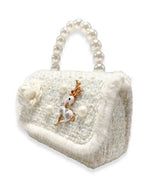 A side and front angle view of a girl's ivory tweed purse with a large pearl handle, the front flap has white fur around the edge and a tweed ivory flower on the front, with 3 large pearls spaced out around an ivory and gold deer charm.  