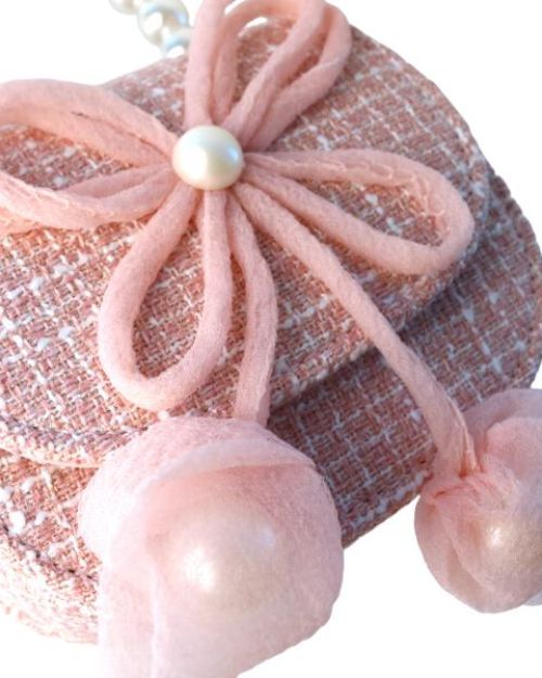 Up close image of a little girls pink tweed pearl handle purse with a large pink thin string bow on the front with a pearl in the middle of the bow.