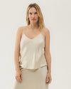 A light beige silk camisole with thin straps, a gentle v-neckline, and a draped fit. The camisole is paired with a matching skirt.