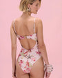 Back view of a pink floral print bodysuit featuring an open-back cutout design, adjustable spaghetti straps, and high-leg silhouette on a pink studio background.