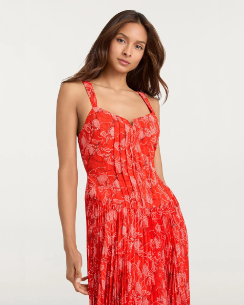 Person wearing a red floral pleated dress with thin straps on a plain background.
