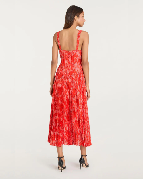 Back view of a person wearing a red floral pleated midi dress with thin straps and black heels on a plain background.