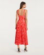 Back view of a person wearing a red floral pleated midi dress with thin straps and black heels on a plain background.