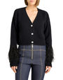 Black cropped cardigan with decorative buttons and feather-trim cuffs, paired with dark denim pants on a plain background.