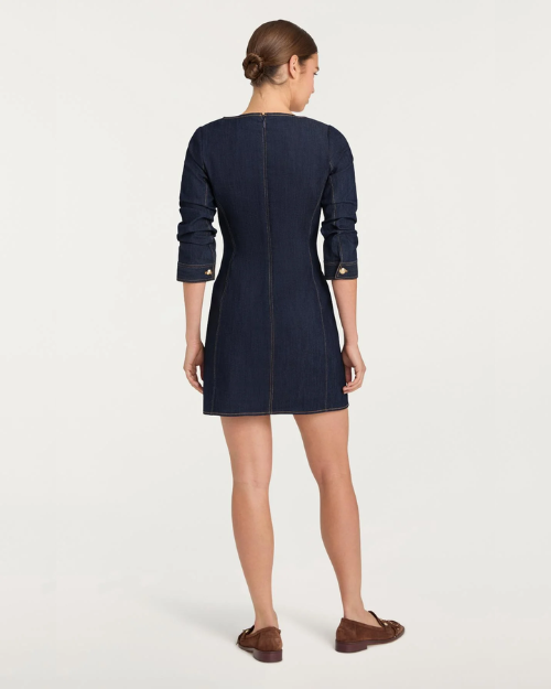 Back view of a person wearing a dark denim button-front mini dress with gold buttons and brown loafers on a plain background.
