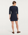 Back view of a person wearing a dark denim button-front mini dress with gold buttons and brown loafers on a plain background.
