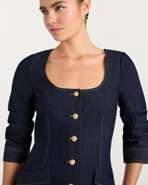 Person wearing a dark denim button-front mini dress with gold buttons on a plain background.
