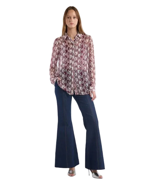 A woman wearing a burgundy and white patterned shirt. flared jeans stands confidently, showcasing her stylish outfit.