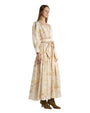 A woman is wearing a long, flowing beige dress with a subtle horse motif print. The dress features long sleeves with gathered cuffs, a V-neckline, and a wide matching belt tied at the waist into a large bow, creating a softly cinched silhouette. 