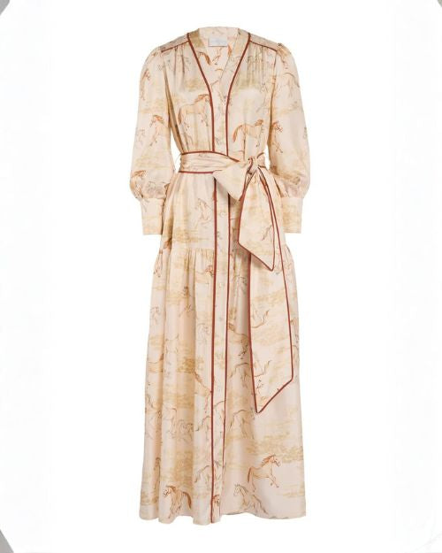 The dress features a subtle horse-themed print throughout the fabric and has a button-down front with vertical contrast piping in a darker tone. It includes long sleeves with gathered cuffs, a V-neckline, and a wide matching belt tied at the waist into a large bow. 