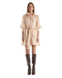 A woman wearing a short beige dress with a subtle horse print pattern and brown knee-high boots. 