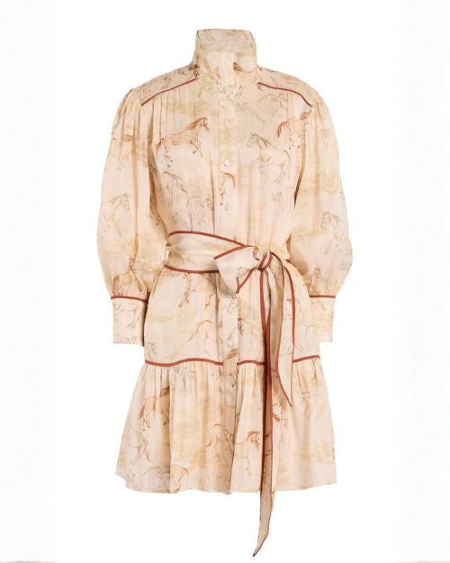 The dress features a subtle horse print pattern throughout and a high stand collar with a button-front closure. It has long sleeves with gathered volume and fitted cuffs. A wide matching fabric belt is tied at the waist into a large bow, accented with contrast piping that also outlines the seams and tiers. 