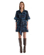 A woman wearing a blue dress and boots stands confidently, showcasing her stylish outfit.