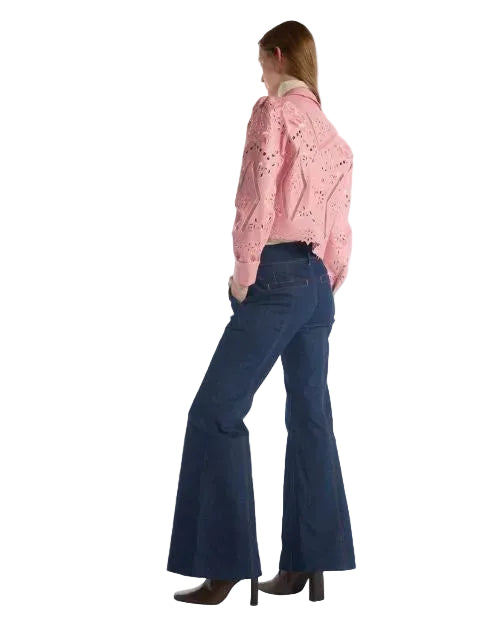 A woman wearing a pink shirt and flared jeans stands confidently, showcasing a casual yet stylish outfit.