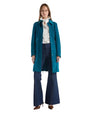 A woman wearing a peacock blue suede coat with wide flared jeans, exuding elegance and refined fashion.