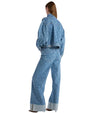 A woman seen from the back, wearing denim pants, standing in a casual pose.