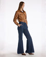 A woman dressed in a leather jacket and flared jeans poses, embodying a trendy and relaxed fashion sense.