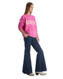 A woman dressed in a pink sweater that has "Houston" printed on it, standing against a neutral background.