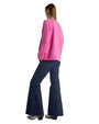 A woman in a pink sweater and flared jeans is seen from the back, showcasing her casual outfit