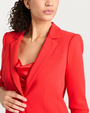 Close-up of a woman wearing a bright red suit with a matching top against a white background.