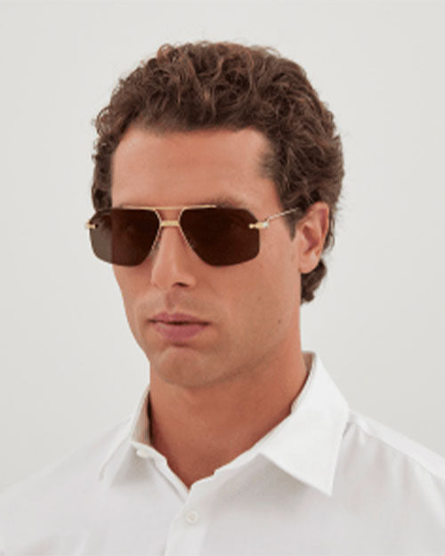 A man in sunglasses and a white shirt stands confidently, showcasing a relaxed and stylish demeanor.
