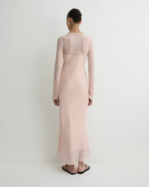 Back view of a blush pink sheer long-sleeve maxi dress with a fitted silhouette and semi-transparent upper back detail