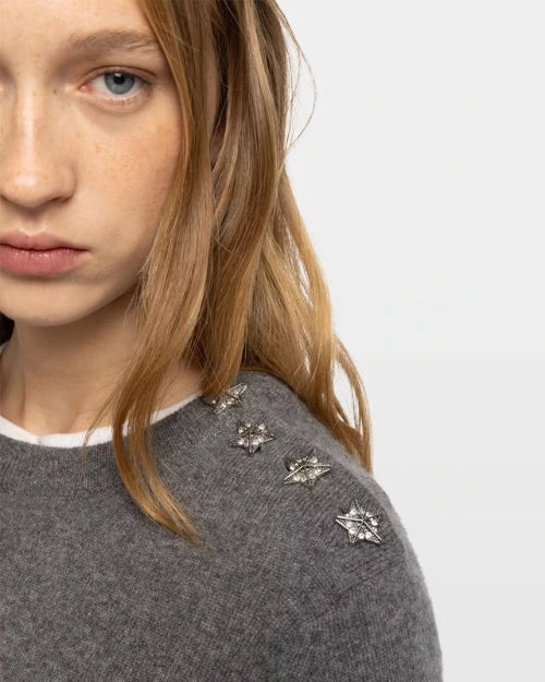 Close-up of gray knit sweater with silver star embellishments on shoulder
