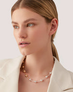 A model showcases a white blazer paired with a necklace that has luminous spheres that are paced out between elongated silver and gold beads. 