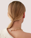 A woman with a ponytail and atwo-tone necklace, exuding elegance in a simple, stylish setting.