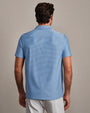Back view of a blue striped performance polo shirt with short sleeves, classic collar, and athletic fit, paired with light gray pants against a neutral background.