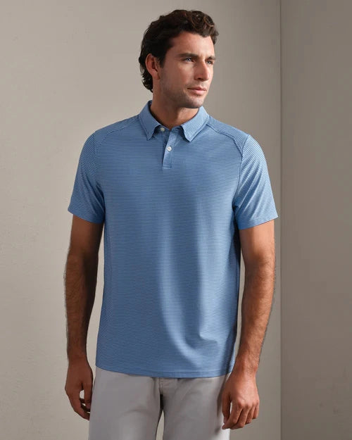 Person wearing a blue striped performance polo shirt with short sleeves and light gray pants, standing in a neutral indoor setting.