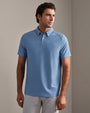 Person wearing a blue striped performance polo shirt with short sleeves and light gray pants, standing in a neutral indoor setting.