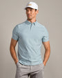 Person wearing a light blue striped performance polo shirt with short sleeves and light gray pants, paired with a white golf cap in a studio setting.