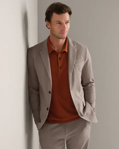 Person wearing a taupe tailored blazer and matching trousers with a rust knit polo shirt, showcasing a modern smart casual outfit.