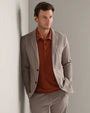 Person wearing a taupe tailored blazer and matching trousers with a rust knit polo shirt, showcasing a modern smart casual outfit.