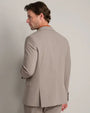 Back view of a men's taupe tailored blazer worn with matching trousers, showcasing the clean silhouette and center back vent.