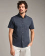 Person wearing a navy short-sleeve button-down shirt with a chest pocket and light-colored pants in a studio setting.