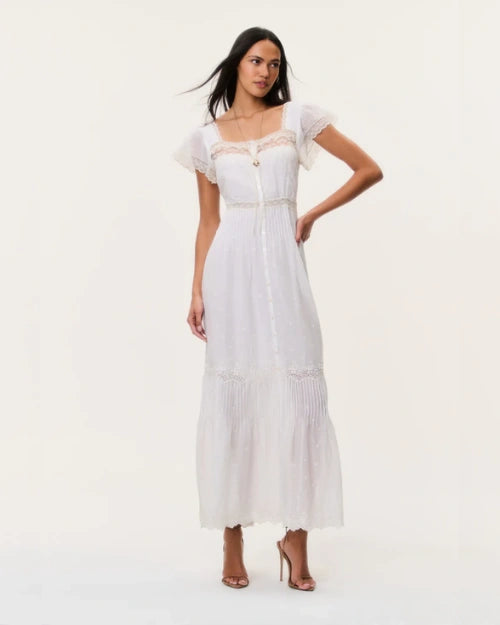 White maxi dress with lace trim detailing, flutter sleeves, button-front design, and a tiered skirt, styled on a neutral studio background.