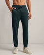 Dark teal jogger pants with a drawstring waistband and tapered fit, styled with white sneakers in a studio setting.
