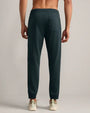 Back view of dark teal jogger pants featuring an elastic waistband, rear patch pocket and tapered cuffed legs, styled with white sneakers.