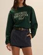 Favorite Daughter Club dark green crewneck sweatshirt with white logo graphic, styled with a navy skort and black leather belt.