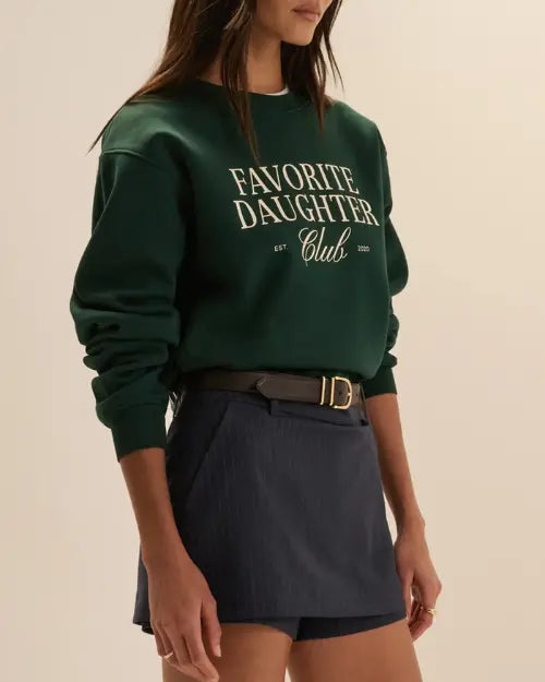 Dark green Favorite Daughter Club crewneck sweatshirt styled with a navy skort and black belt, featuring white graphic lettering on the front.