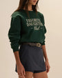 Dark green Favorite Daughter Club crewneck sweatshirt styled with a navy skort and black belt, featuring white graphic lettering on the front.