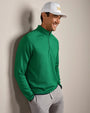 Person wearing a green textured quarter-zip performance pullover with long sleeves, light gray pants, and a white golf cap in a lifestyle setting.