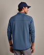 Back view of a blue textured quarter-zip performance pullover with long sleeves, athletic fit, and mock neck collar, paired with gray pants and a navy cap.
