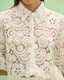 White crochet lace blouse with high neck tie detail, long sleeves, floral lace pattern, and semi-sheer vintage-inspired design.