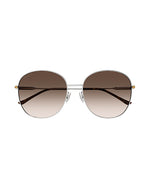 Front view of round-framed sunglasses with a thin silver metal frame with brown lenses. The sunglasses have tortoiseshell colored earpieces and small gold accents.
