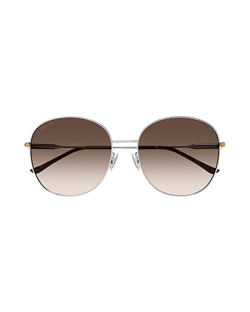Front view of round-framed sunglasses with a thin silver metal frame with brown lenses. The sunglasses have tortoiseshell colored earpieces and small gold accents.