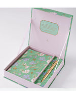 Gift box with a floral-patterned journal and a gold pen. The box lid is open, revealing a heartfelt quote. The tone is elegant and inviting.